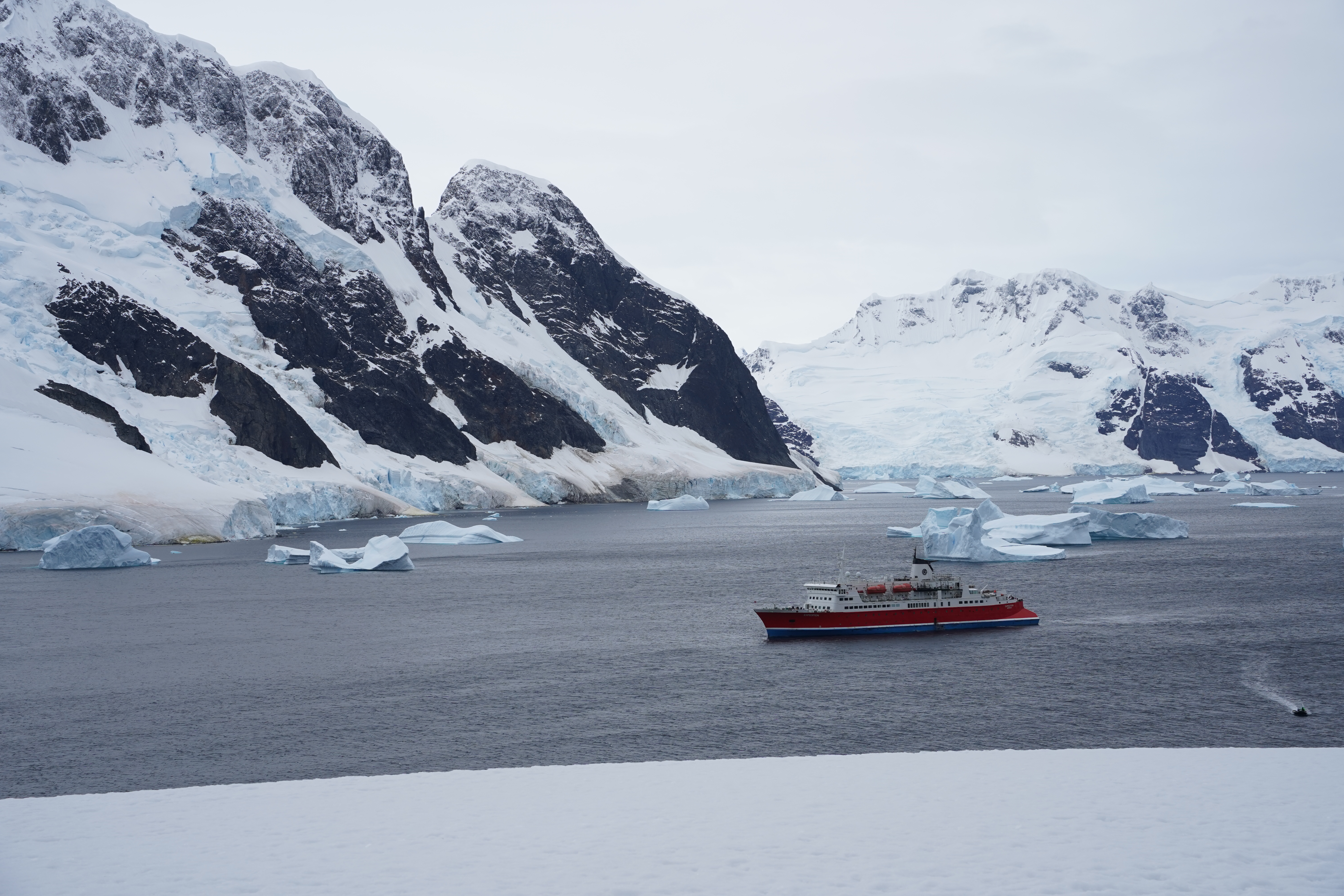 A red and white small cruise ship sits in the water off the coast of Antarctica