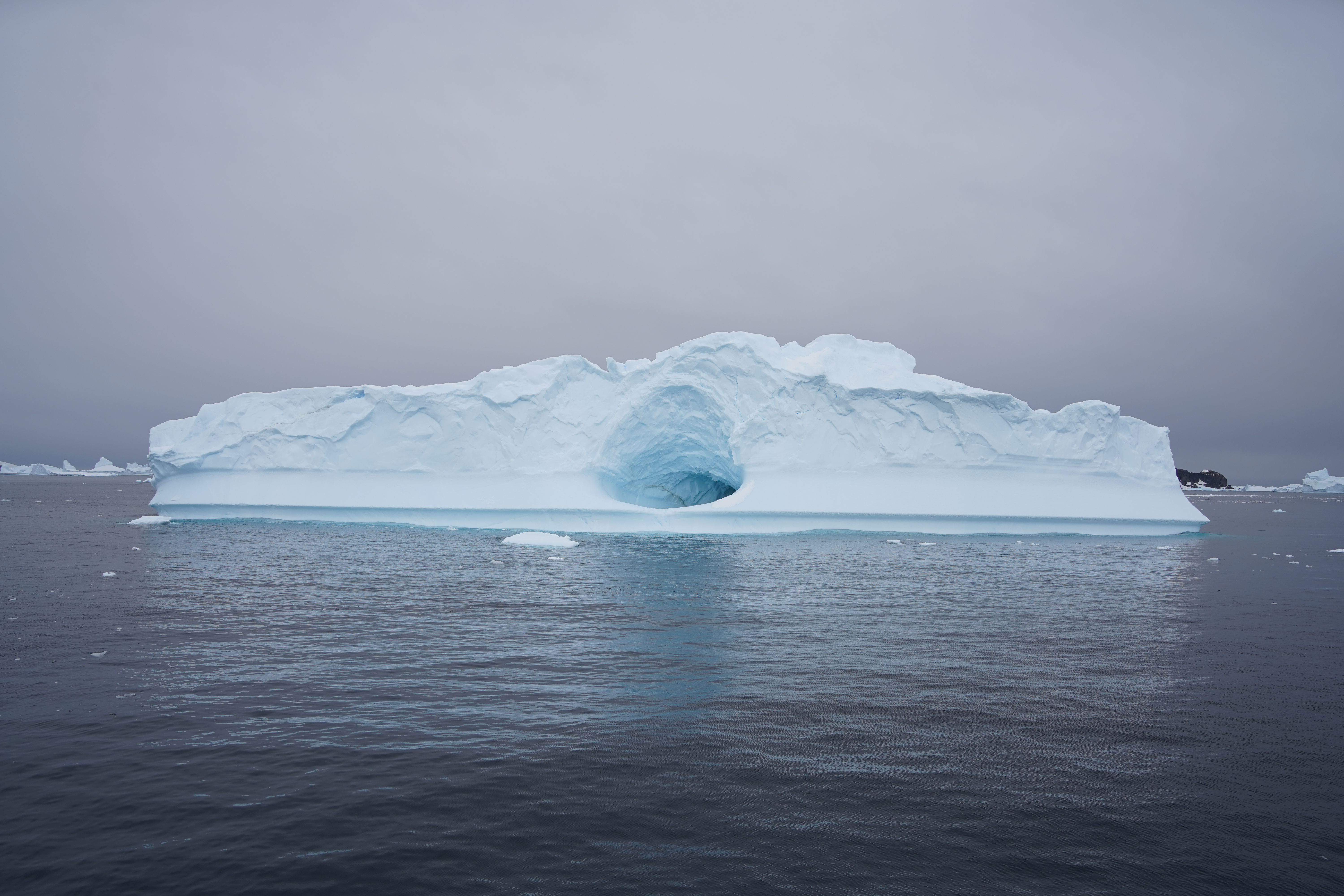 A glacier floating in the waters of Antarctica. It has a massive whole in the center of it.
